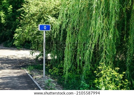 0 Zero kilometer road sign on the bystreet. Blue mark with information about mileage beginning of the path on green nature blur background.