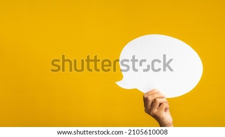 A speech bubble concept. Hand holding of an empty white speech balloon on yellow background with copy space for text. Close-up photo