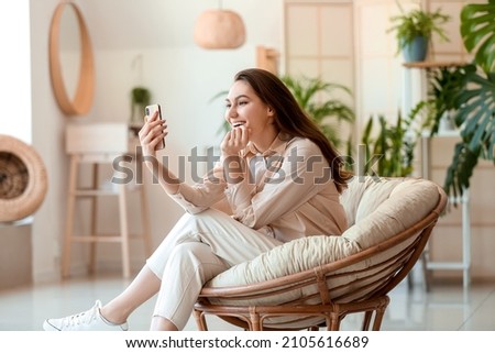 Young happy woman taking selfie in armchair