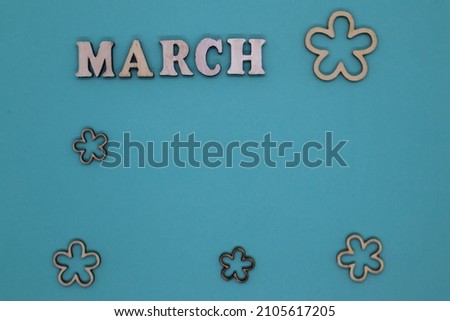 Spring concept. Wooden letters March and small wooden flowers on a blue background. Top view. Flat lay. Mockup.