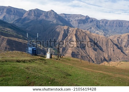The electricity station is high in the mountains. Poles with wires for electricity in rural mountainous areas. Electricity in the village. Mountains and blue cloudy sky.