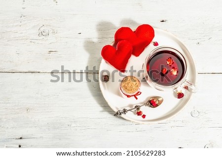 Hibiscus tea. The healthy hot organic drink is served in glass cups. St.Valentine's symbols as hearts, rose petals, and sweet sugar candies. Hard light, dark shadow, white wooden background, top view