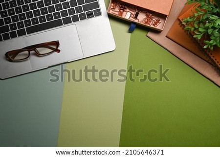 Computer laptop, books, potted plant and eyeglasses on green background.