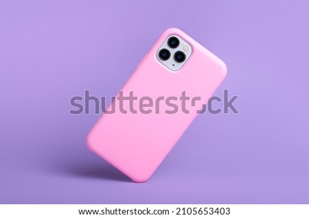 Smartphone iPhone 11 and 12 Pro max in pink silicone case falls down back view, phone case mockup isolated on purple background Royalty-Free Stock Photo #2105653403