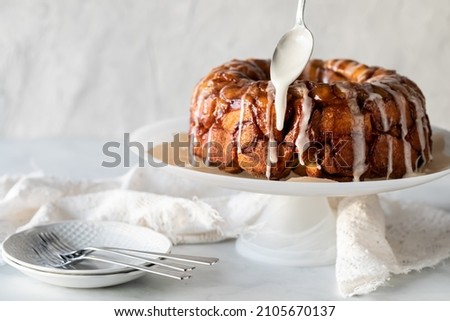Apple cinnamon monkey bread on a pedestal stand with icing being drizzled on top