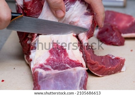 The butcher cuts beef meat on a cutting board with a knife. Butcher's hands and meat on the table. The butcher separates the entrecote.