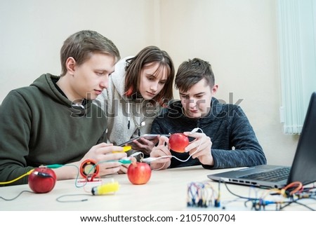 School experiment with apples. School students extract electricity from apples, use of the energy of a chemical reaction. Learning at table STEM and STEAM engineering science education class. Royalty-Free Stock Photo #2105700704