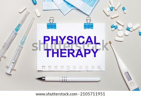 On a light gray background, blue medical masks, syringes, an electronic thermometer, pills, a pen and a notebook with the inscription PHYSICAL THERAPY. Medical concept