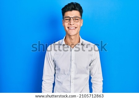 Young hispanic man wearing casual clothes and glasses looking positive and happy standing and smiling with a confident smile showing teeth  Royalty-Free Stock Photo #2105712863