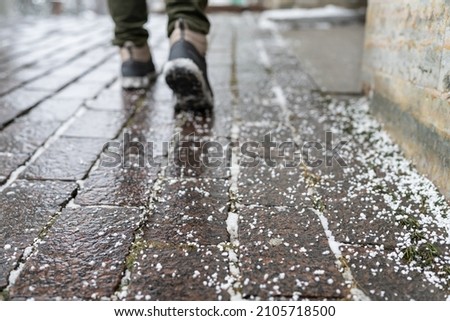 Selective focus on technical salt grains on icy sidewalk surface in wintertime, used for melting ice and snow. Applying salt to keep roads clear and people safe in winter weather from ice or snow Royalty-Free Stock Photo #2105718500