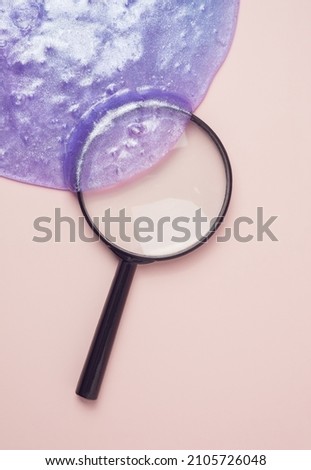 Violet slime covering a magnifying glass on a pastel pink background. Search for alien life minimal concept.