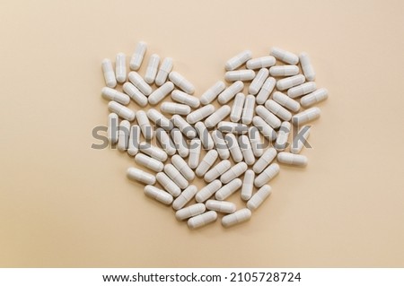 capsules of white color on a beige background, laid out in the shape of a heart Royalty-Free Stock Photo #2105728724