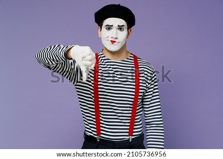Frowning upset distempered unnerved young mime man with white face mask wears striped shirt beret showing thumb down dislike gesture isolated on plain pastel light violet background studio portrait Royalty-Free Stock Photo #2105736956