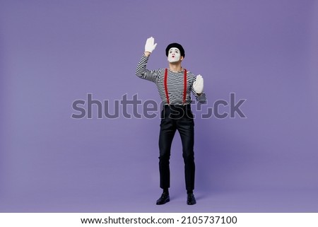 Full size body length young mime man with white face mask wear striped shirt beret look up stand hands raised like touch invisible wall isolated on plain pastel light violet background studio portrait Royalty-Free Stock Photo #2105737100