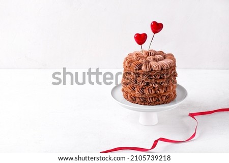 Chocolate cake with coffee cream topped with two heart decorations served on the cakestand. Valentines day dessert. Copy space Royalty-Free Stock Photo #2105739218