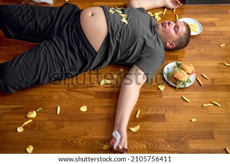 Overweight boy sleeping on floor surrounded by fast food, overeating. obese caucasian teenage boy in casual wear is lazy, spend rest time after school alone. healthcare, weight loss concept
