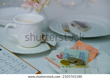 close-up on white plate with euro bills and coins, selective focus, cup of coffee, dishes with food, lunch concept in restaurant, cafe, tip money concept, change of waiter