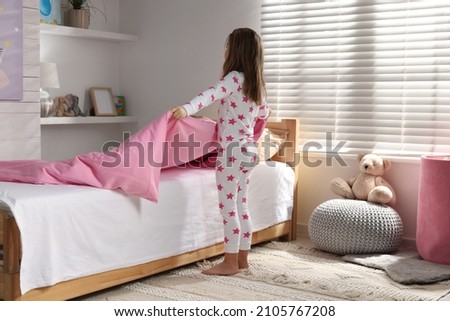 Cute little girl making bed at home Royalty-Free Stock Photo #2105767208