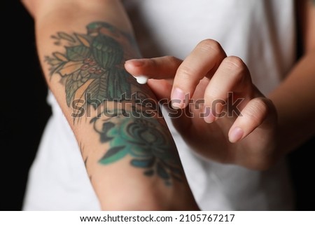 Woman applying cream on her arm with tattoos against black background, closeup Royalty-Free Stock Photo #2105767217