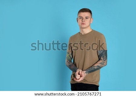 Young man with tattoos on light blue background. Space for text