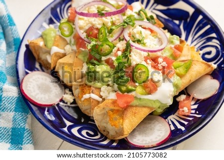 Traditional mexican fried potato tacos called flautas with guacamole and cheese