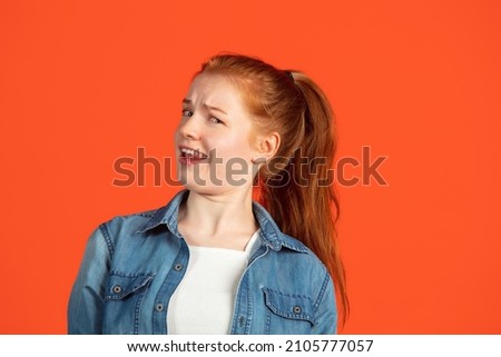 Mistrustful look. Half-length portrait young girl isolated over red background. Model in casual clothes. Concept of human emotions, facial expression, beauty. Copy space for ad Royalty-Free Stock Photo #2105777057