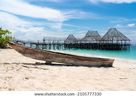 Closed restaurant building on the background. Small native's fishing boat in the front on a perfect white sandy beach. Amazing construction frame on the background leaping out into the ocean