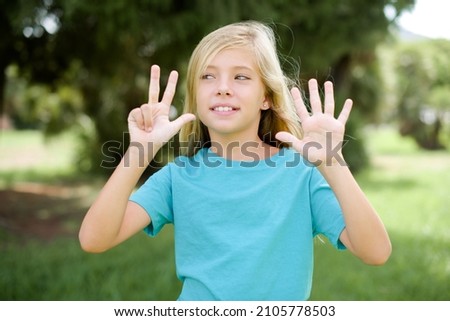 caucasian little girl wearing blue t-shirt standing outdoors showing and pointing up with fingers number eight while smiling confident and happy.