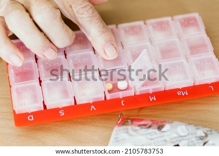 Organizer of daily pills for taking medicine for older people. Reminder for sick patients with regular pill treatments Translation:  “M T W T F S S Breakfast, lunch, dinner” Royalty-Free Stock Photo #2105783753