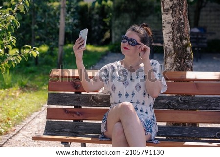 Young woman tourist taking a selfie on a bench in a botanical garden with sunglasses in the sunshine
