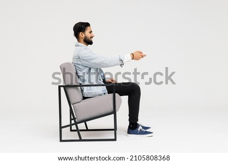 Side view of Asian man sitting in the armchair while watching TV in the studio Royalty-Free Stock Photo #2105808368