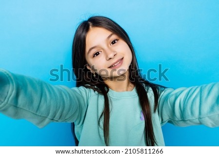 Portrait of friendly caucasian little girl over blue background taking selfie