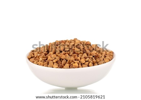 Uncooked organic buckwheat groats in a white ceramic saucer, close-up, isolated on white.