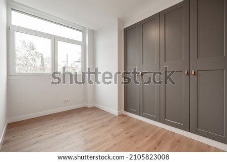 Nice room with large window, pine wood floors and built-in wardrobes with gray doors Royalty-Free Stock Photo #2105823008