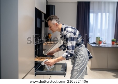 Profile of man putting baking sheet in oven Royalty-Free Stock Photo #2105824406