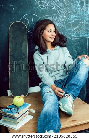 young cute teenage girl in classroom at blackboard seating on table smiling, modern hipster concept