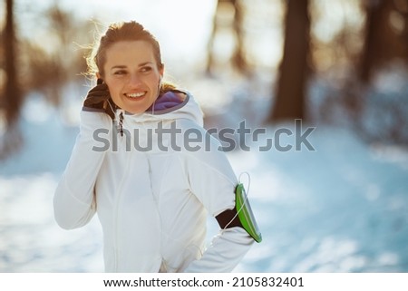 smiling healthy woman in white jacket with headphones outdoors in the city park in winter.