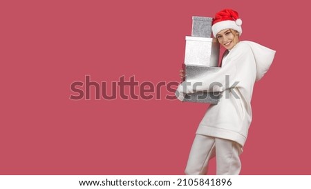 a young woman in a Santa hat smiling hugs her gifts
