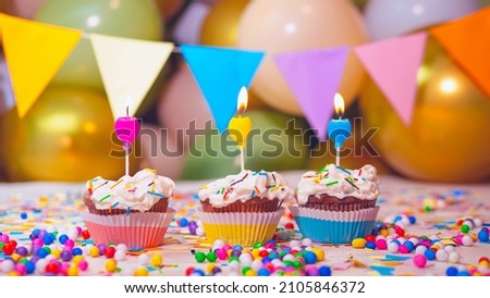 Multi-colored cupcakes with cream with a candle on the background of balloons, happy birthday festive background. Decorations for the holiday