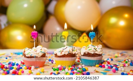 Cupcakes multicolored with cream with a candle in the background balloons, festive background happy birthday
