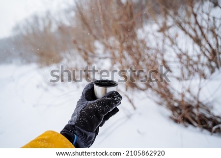A hand holds a mug of hot tea. Drink tea in nature. A glass of hot coffee in the forest. High quality photo