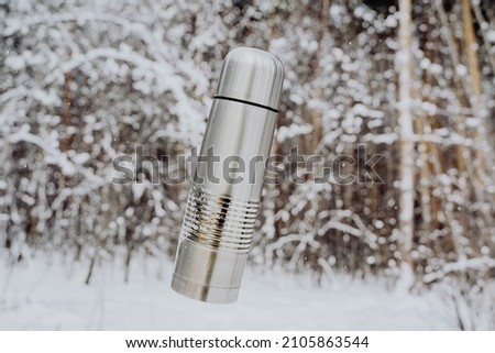 The thermos flies in the air. Vacuum bottle concept. Winter landscape. Metal flask for hot tea. High quality photo