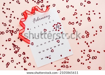 Valentine's Day. Small red hearts highlight the date February 14 on a calendar sheet and a red ribbon on a pink heart-strewn background. Top view