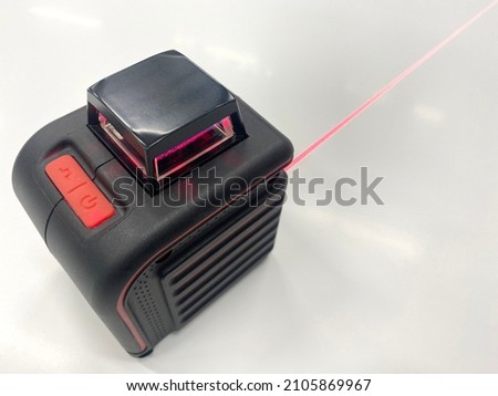 A square electronic laser level shines with a red beam on a white isolate