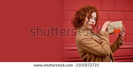 long-awaited gift for valentine's day. lovely wavy-haired girl holding in hands gift box on bright red color background