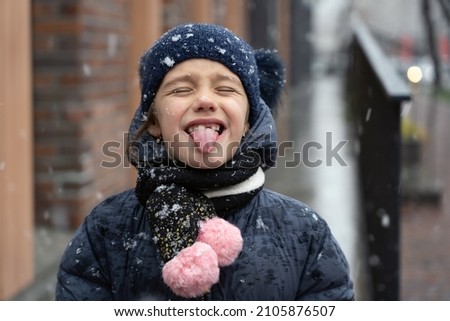 Adorable little girl catching snowflakes with her tongue in  winter city during snowfall. Outdoors winter activities for kids.
