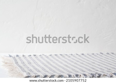 Blue and white striped fabric placemat with empty space for product placement or text. White table and concrete , textured wall. Modern, farmhouse kitchen or dining room.