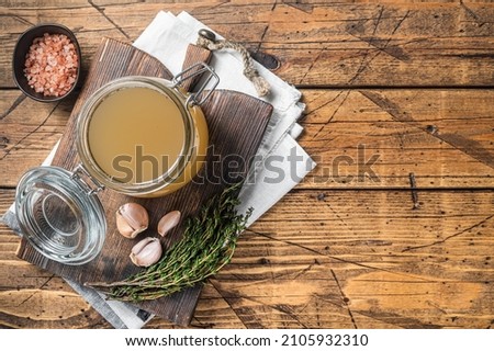 Bone broth for chicken soup in a glass jar. Wooden background. Top view. Copy space