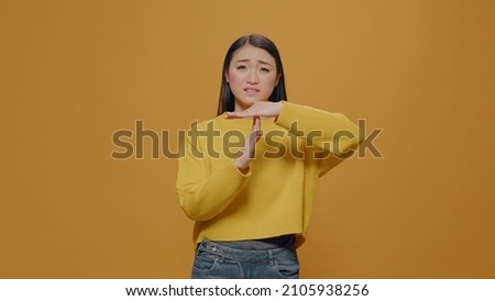 Tired woman doing timeout and break gesture in studio, expressing t shape sign with hands to pause action. Serious person gesticulating refuse and need to finish. Concept of restriction