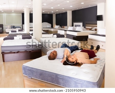 Young hispanic couple sleeping sweetly on comfortable mattress in furniture store
